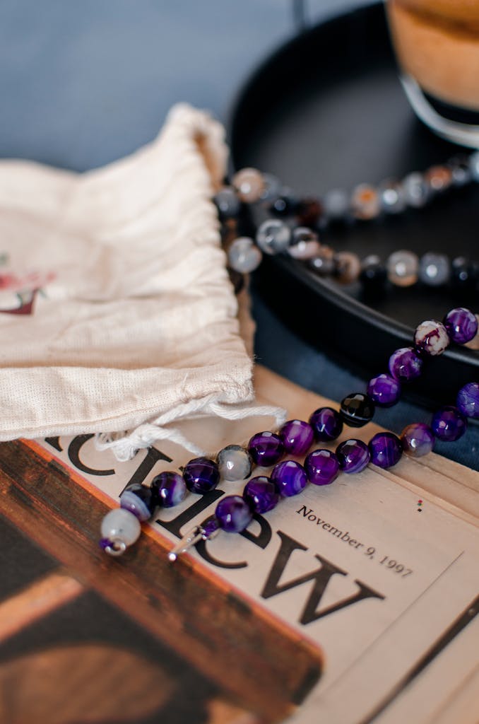 From above of bright purple beads on ceramic plate and newspaper near small cloth bag